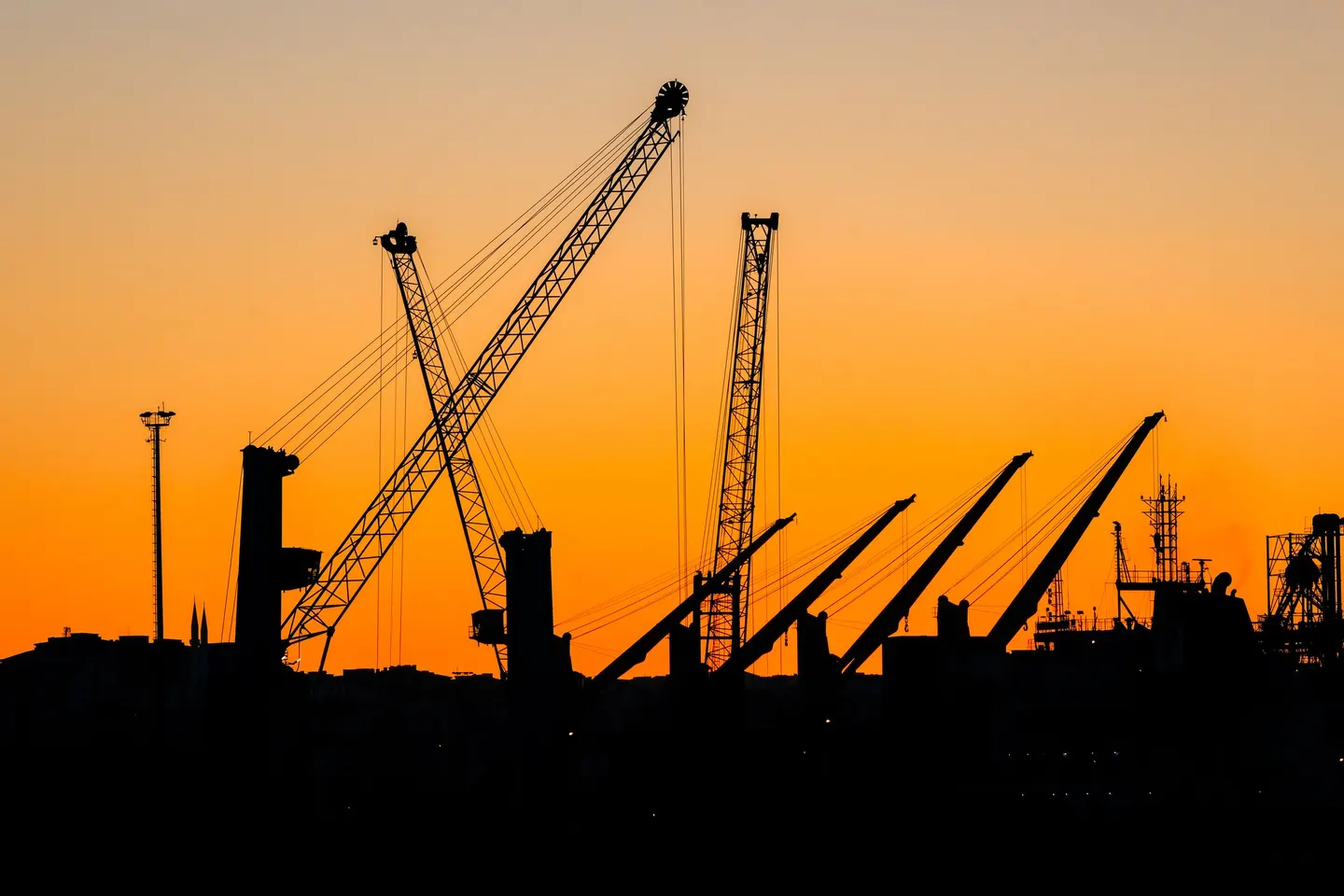 Silhouetted construction cranes against a vivid orange sunset skyline